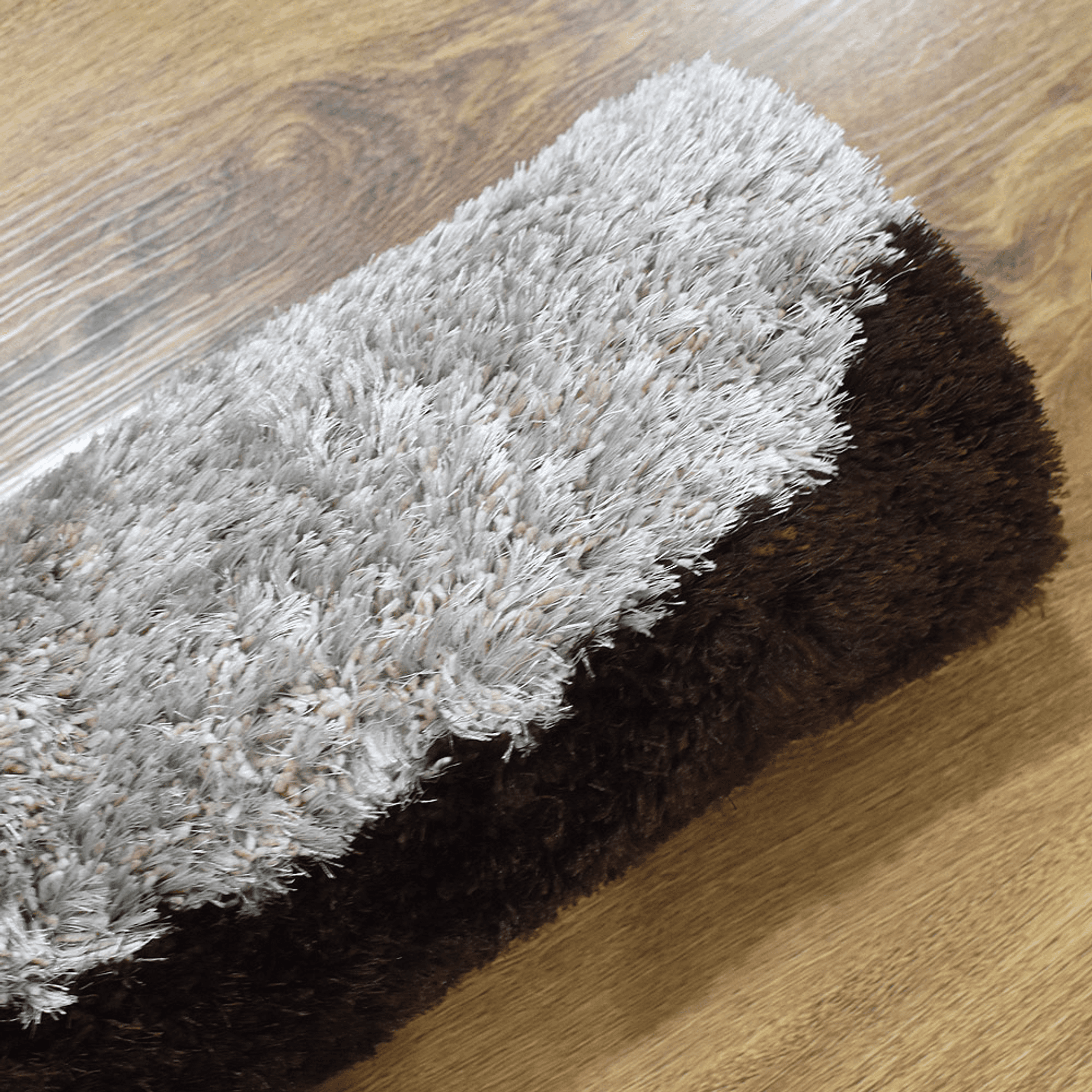 Shag rug corner view with white pile top and dark brown underside along edge