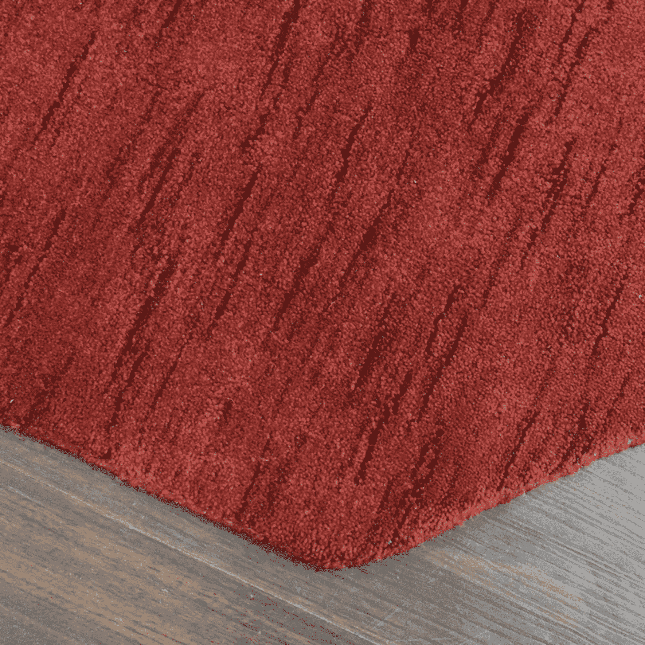 Red rug corner with short pile and faint striated texture, angled view