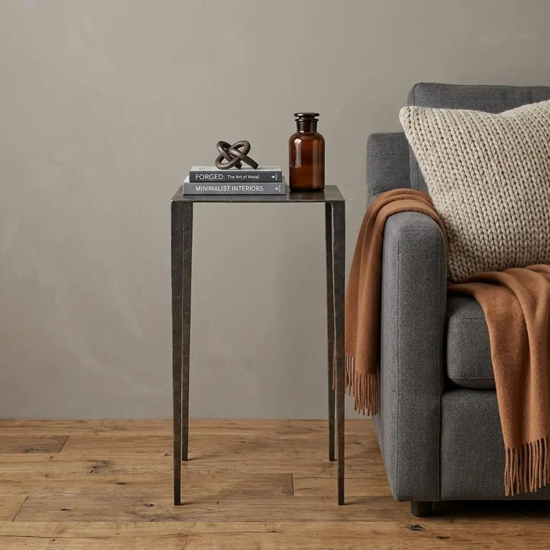 Black metal side table with sleek design, accented by a cozy beige throw and decorative items, perfect for modern minimalist decor.