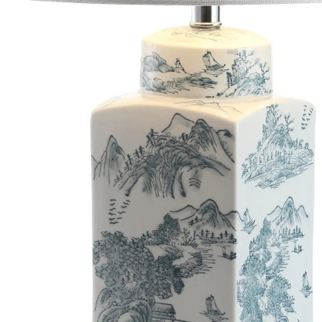 Blue and white porcelain lamp with a scenic mountain design, featuring a coordinating fabric shade.