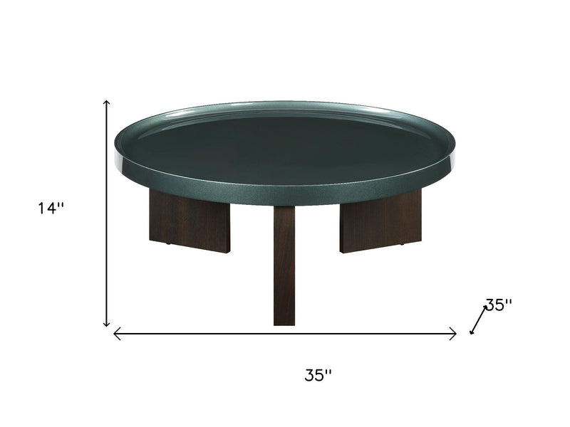 Round coffee table with dark green top and oak wood support legs