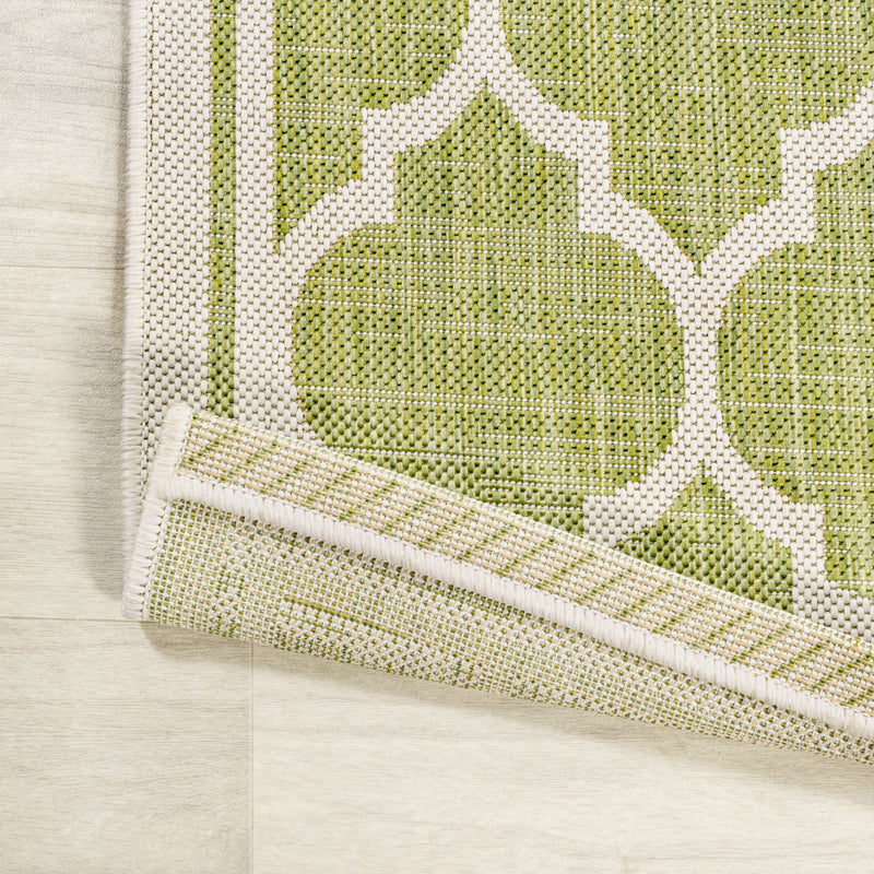 Green and cream area rug corner with border trim and quatrefoil pattern close-up.