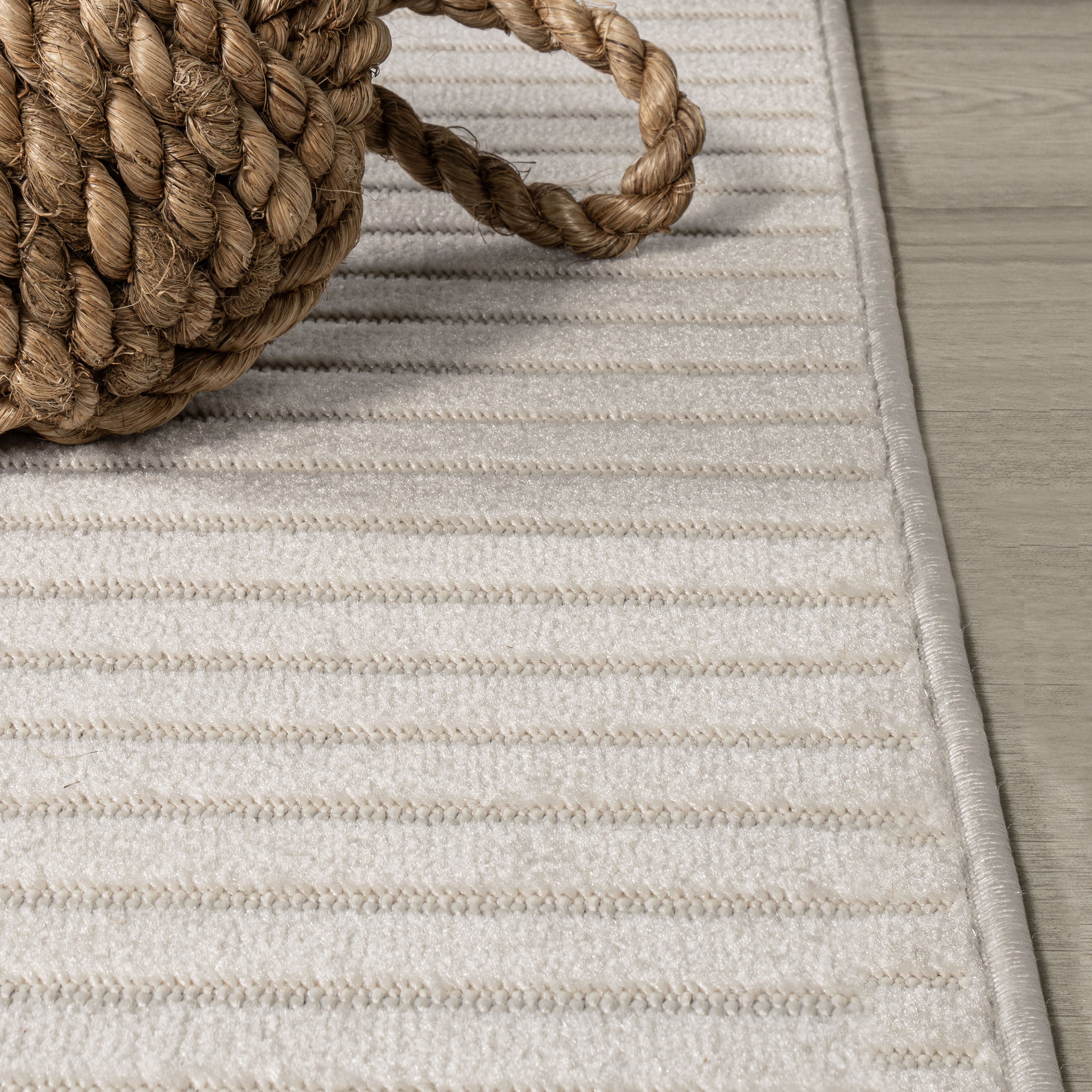 Ivory rug close-up with braided corner loop and thin horizontal stripe texture