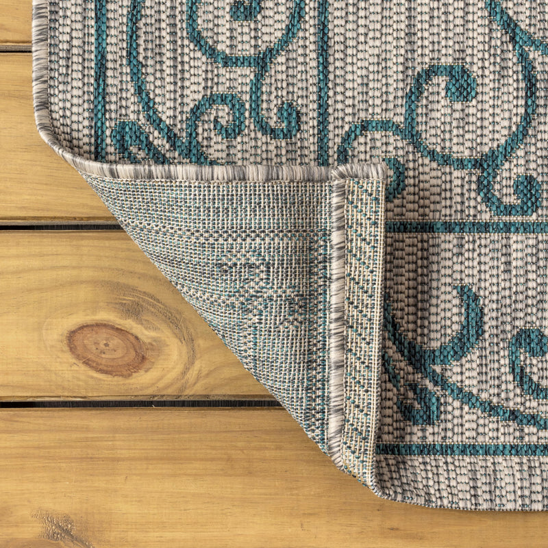 Square area rug corner with gray woven texture and teal scrolling medallion motif.