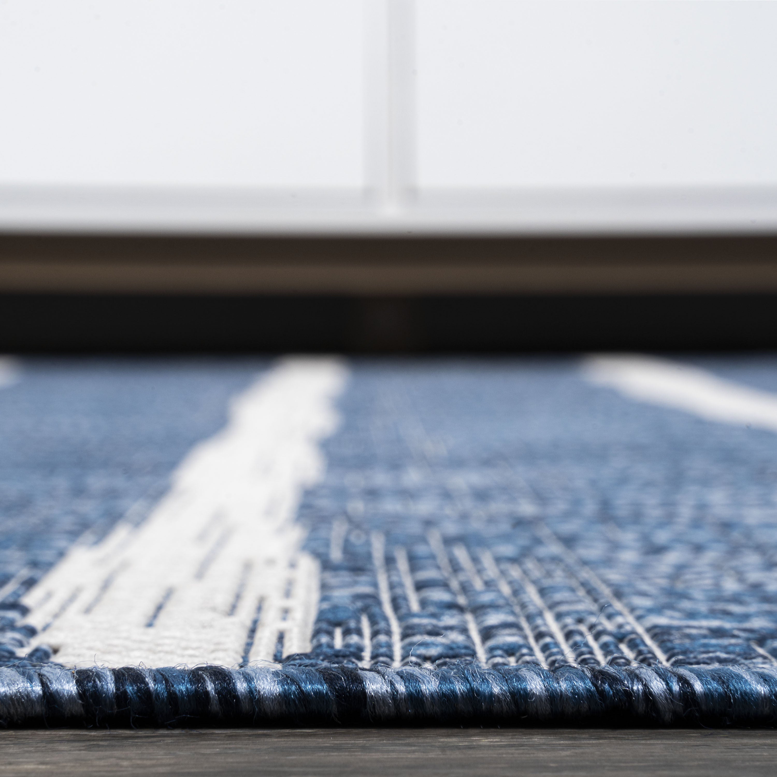 Blue and ivory striped area rug edge with dark binding and looped pile texture
