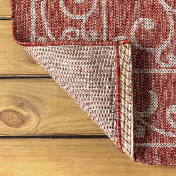 Indoor/outdoor area rug corner with red ground and beige medallion pattern; bound edge