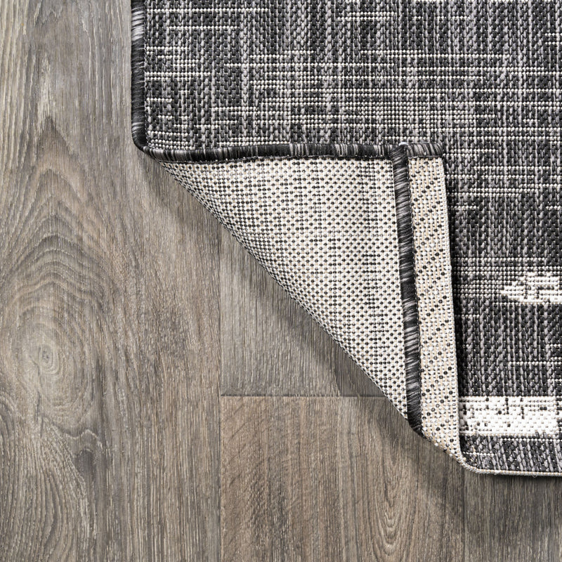 Round rug corner with black edge trim and ivory underside showing on wood floor