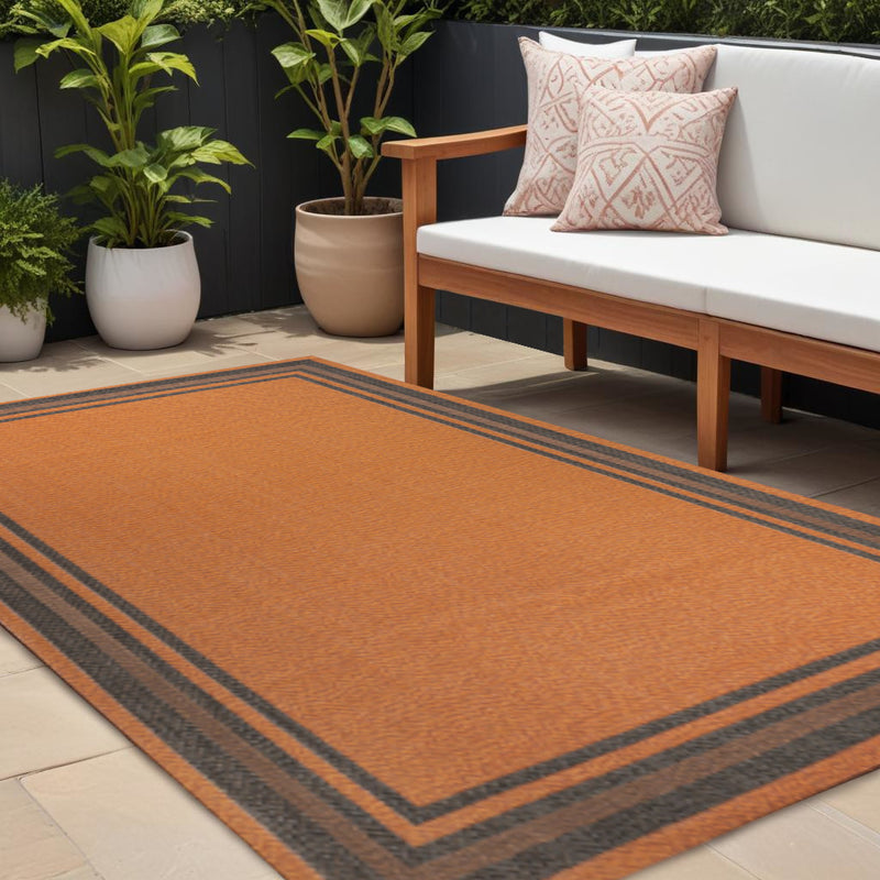 Indoor outdoor area rug, orange center with dark gray striped border