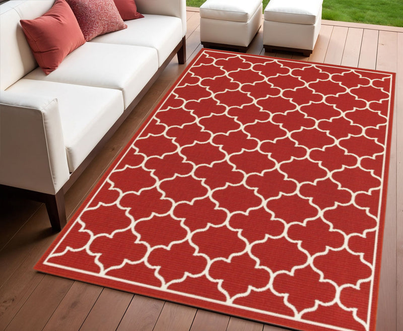 Red outdoor area rug with repeating ivory quatrefoil trellis pattern and border trim