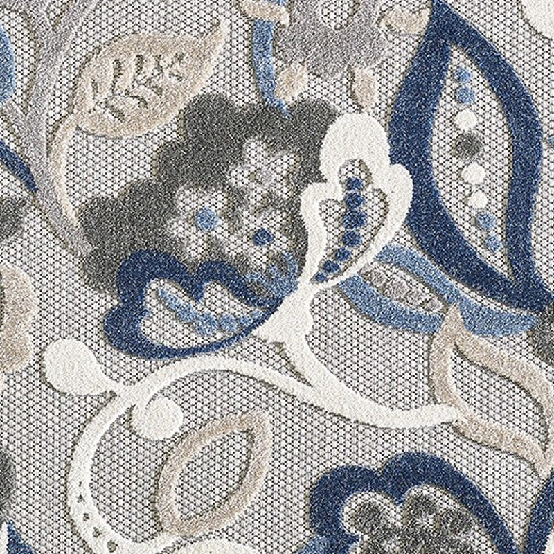 Close-up indoor/outdoor area rug pattern with blue floral clusters and gray accents on light base