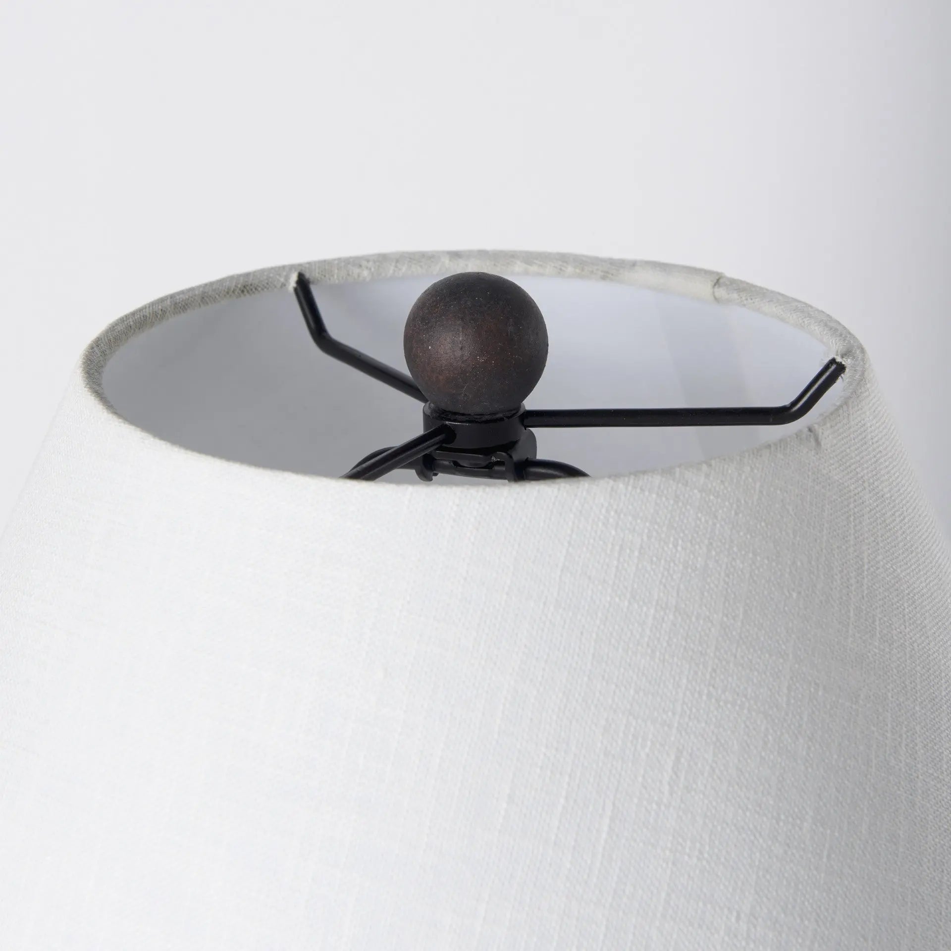 White textured lampshade with a black metal spider fitting and a round bronze finial top.