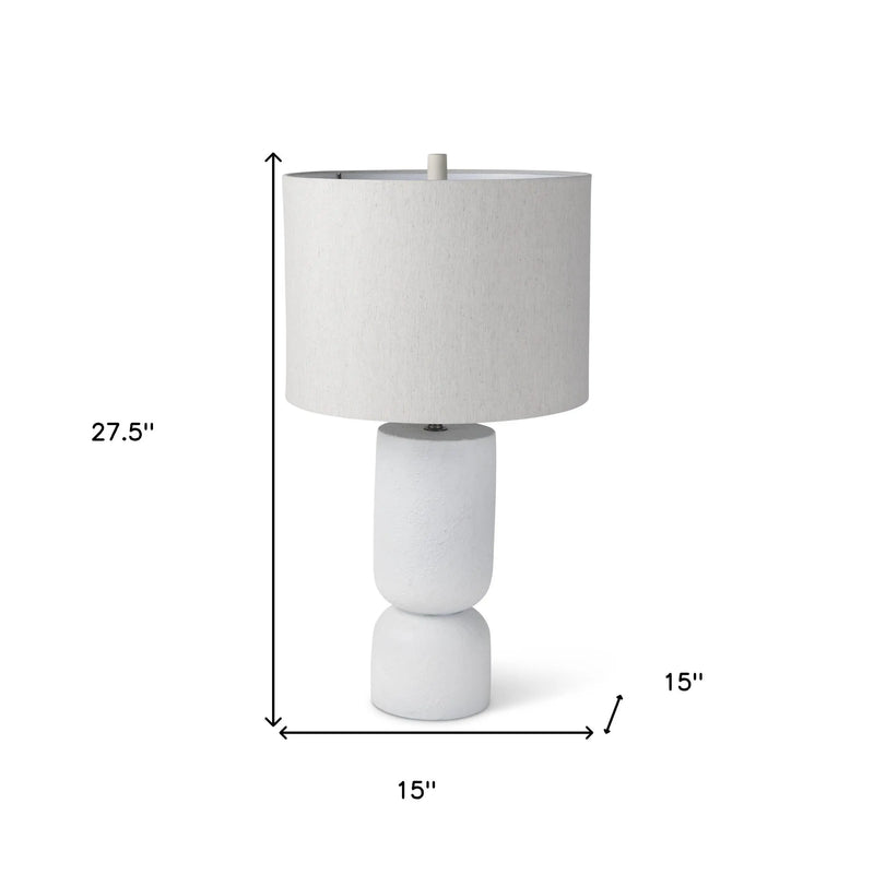 White ceramic table lamp with a textured base and a natural fabric shade, measuring 27.5" tall and 15" wide.
