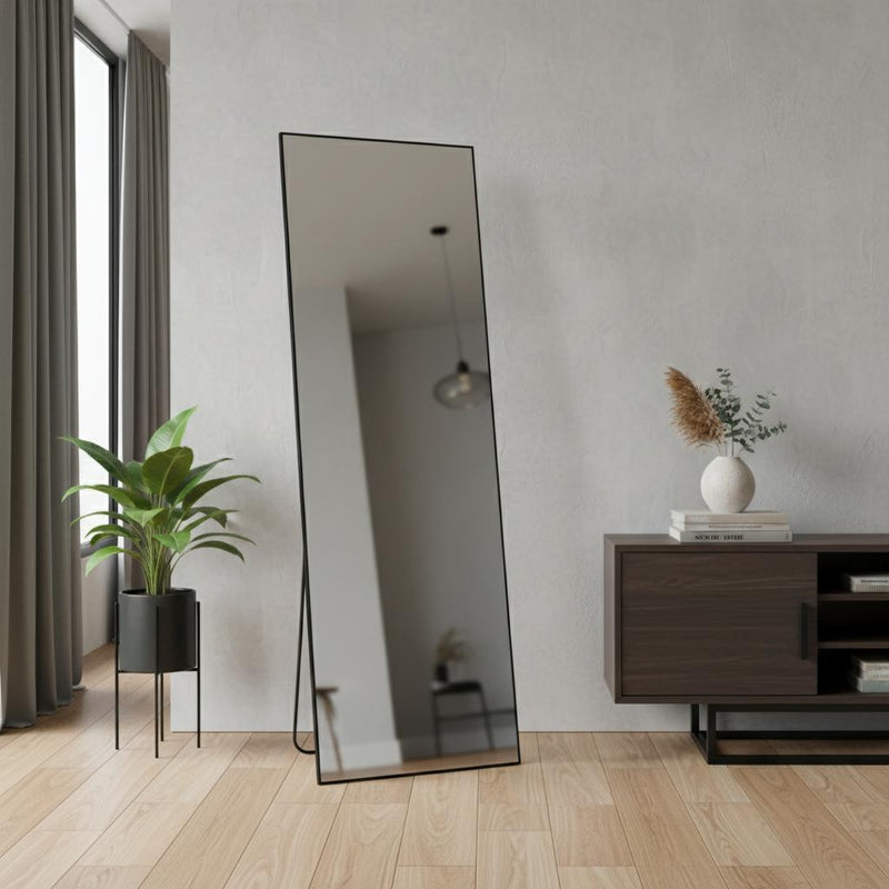 Black metal framed standing mirror leaning against wall in modern room setting