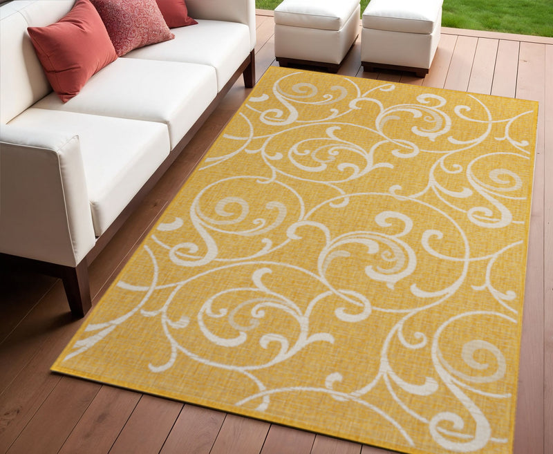 Yellow and cream floral swirl area rug on outdoor wooden floor.