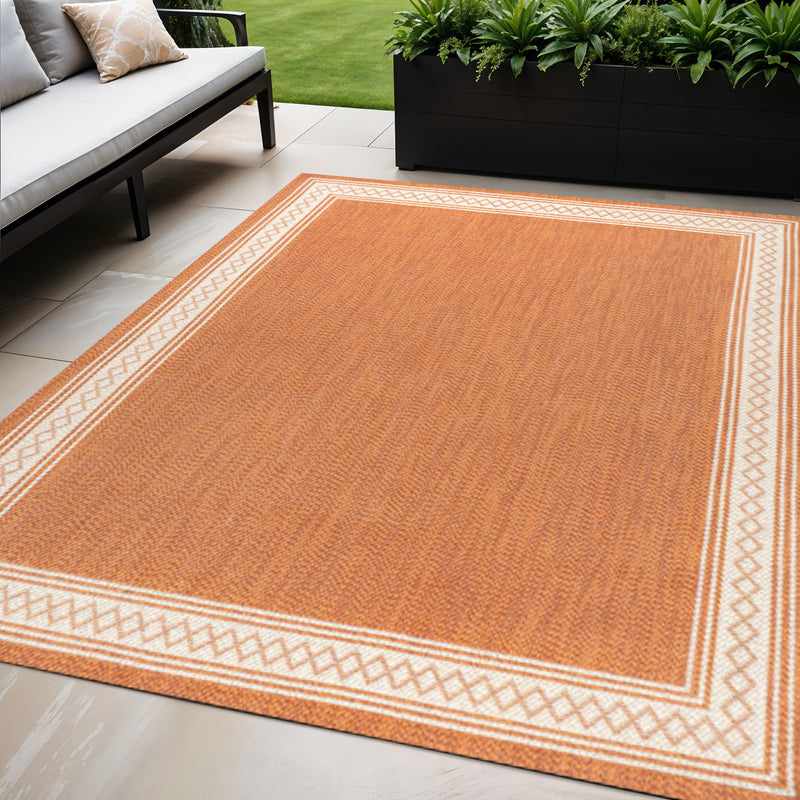 Rectangular orange area rug with cream border and geometric edge pattern, indoor/outdoor