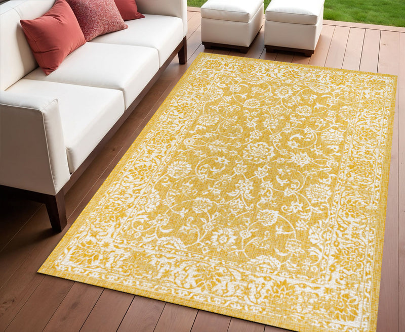 Yellow and cream indoor/outdoor area rug with medallion damask pattern on wood floor
