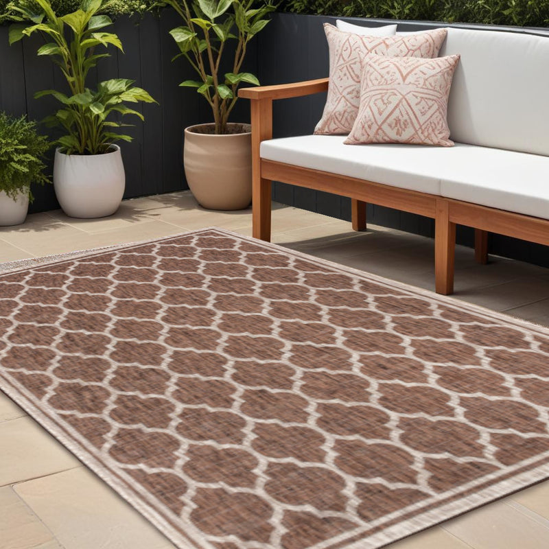 Indoor outdoor area rug with espresso-brown geometric pattern and taupe border on patio