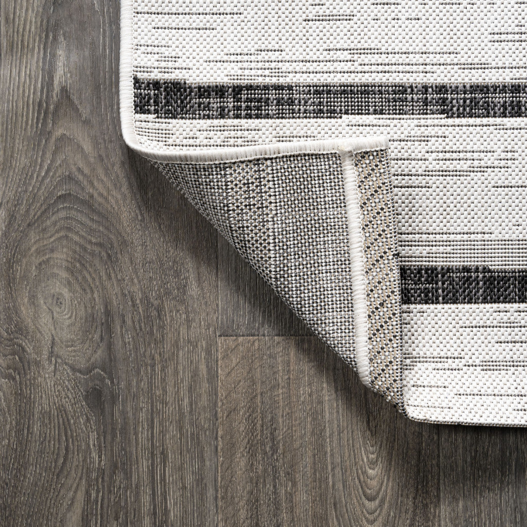 Corner of ivory and black striped area rug with stitched border