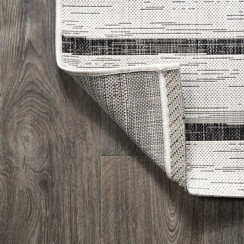 Corner of ivory and black striped area rug with stitched border