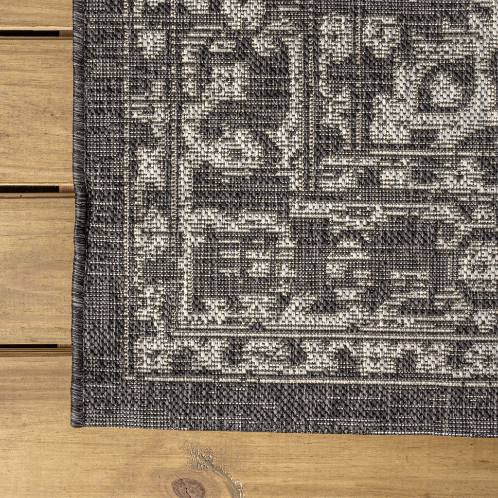 Corner view of black and gray medallion area rug with decorative border