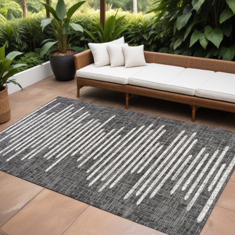 Indoor/outdoor area rug with dark charcoal base and ivory linear stripes, angled view