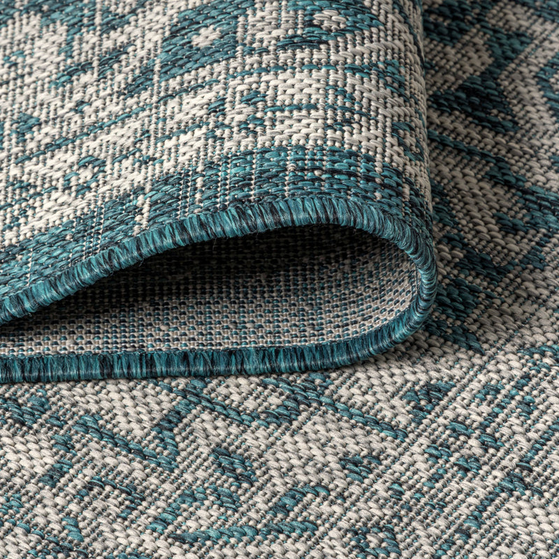 Round area rug rolled edge showing teal binding, textured weave, blue and gray pattern