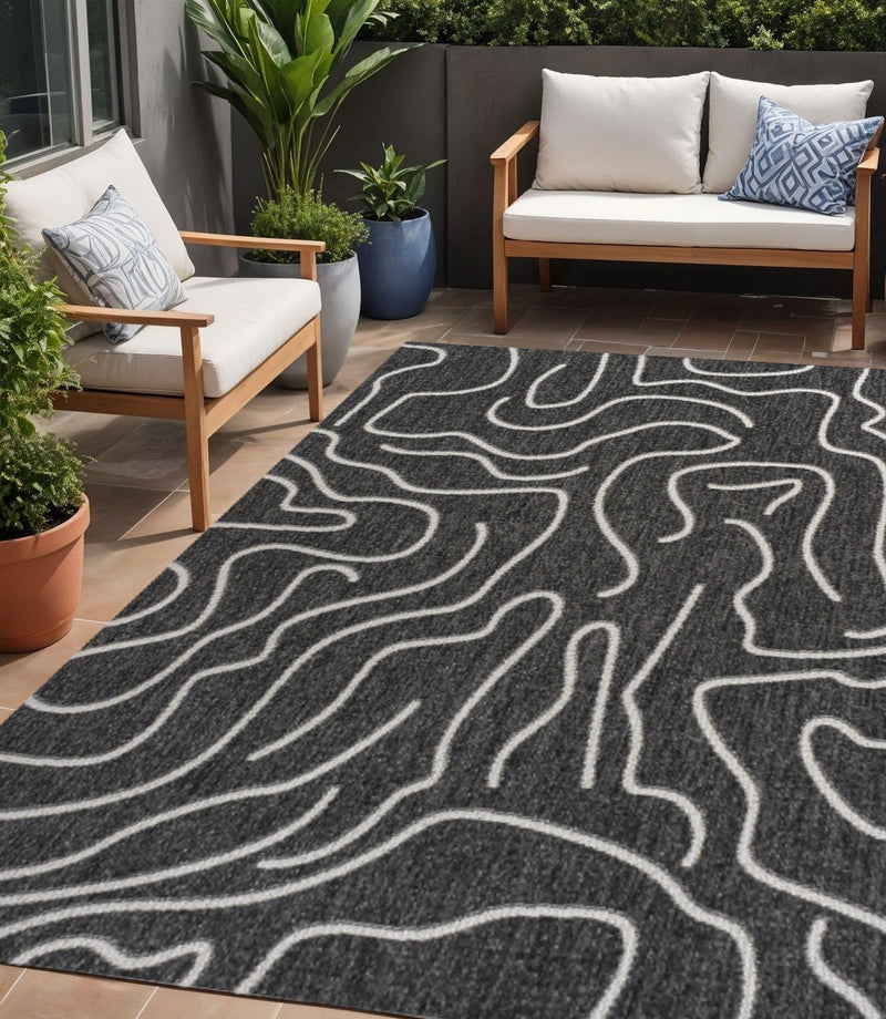 Indoor outdoor area rug with black base and cream wavy abstract lines