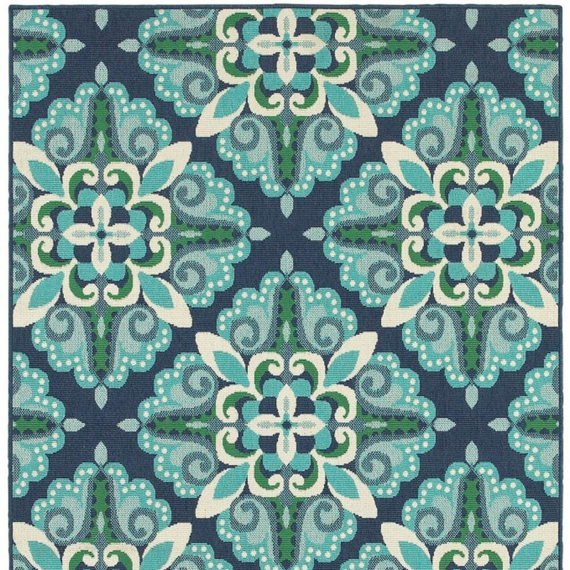 Indoor outdoor area rug repeating floral pattern in teal, green, and cream on navy