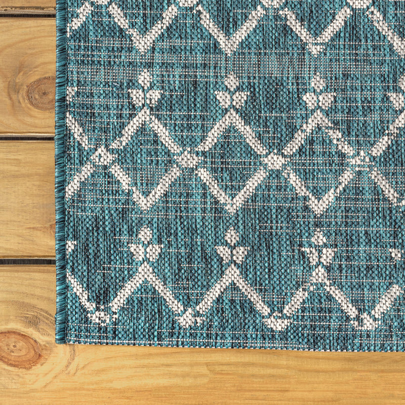 Teal blue area rug corner with white diamond trellis and teal serged edge
