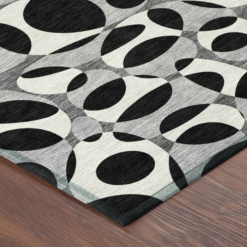 Round abstract area rug with black oval motifs on gray and cream, placed on wood floor