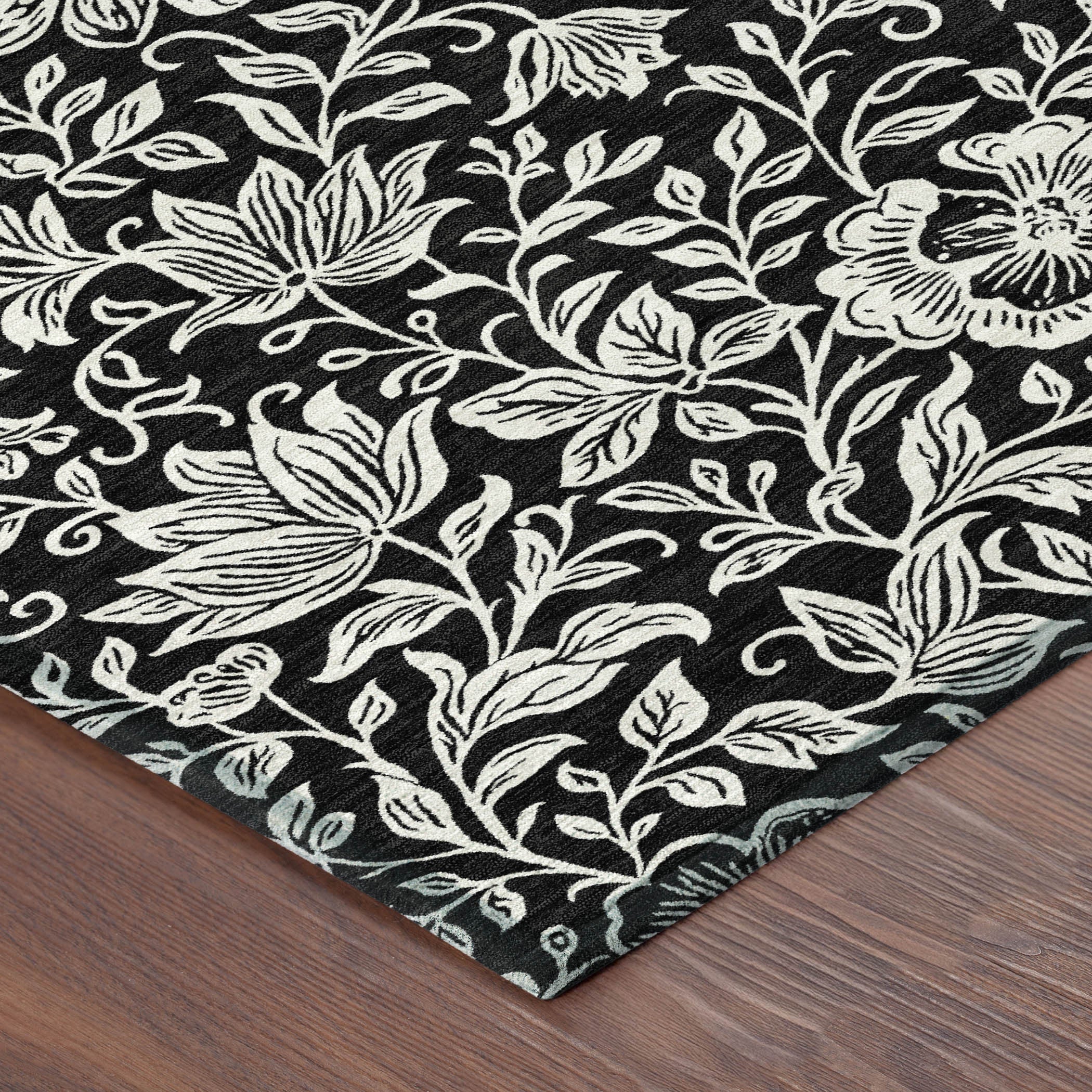 Corner of black and ivory floral area rug with botanical vine and flower design