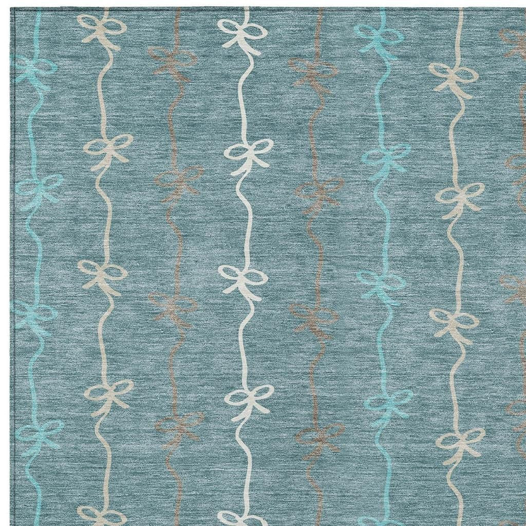 Teal area rug with a playful bow pattern in cream and light brown, made from soft, durable synthetic fibers.