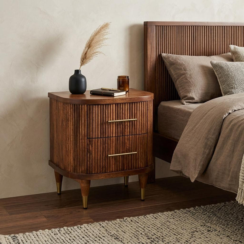 Amber ribbed wood nightstand with two drawers and brass bar pulls beside a bed
