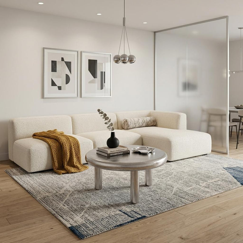 Round silver coffee table with brushed metal top and four short straight legs