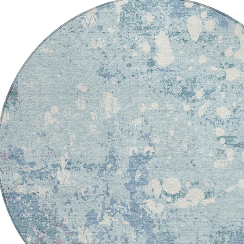 Round light blue rug with beige abstract splatter pattern and low pile texture.