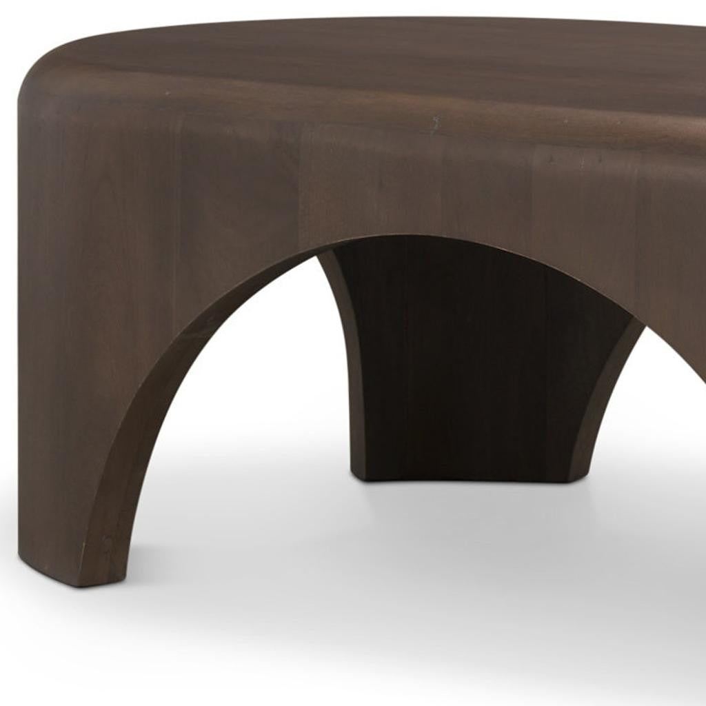 Brown oval solid-wood coffee table with curved cutout base and arched legs.