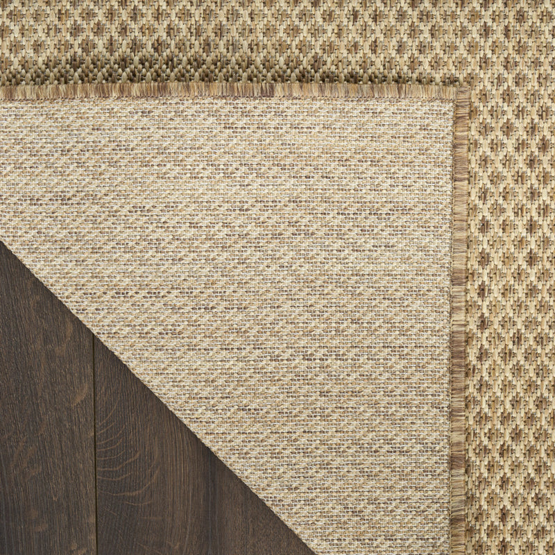 Tan geometric area rug corner with fringed binding and flat woven surface