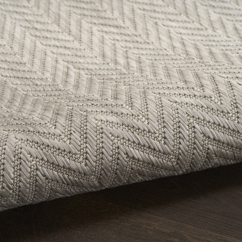 Light gray area rug edge with woven chevron texture and bound border
