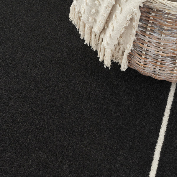 Black and ivory area rug with ivory border stripe and short cream fringe at corner.