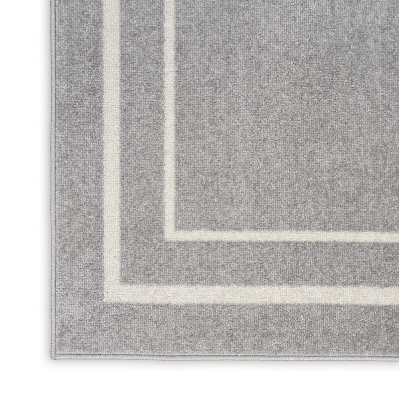 Indoor/outdoor area rug corner close-up with grey pile and ivory border strip.