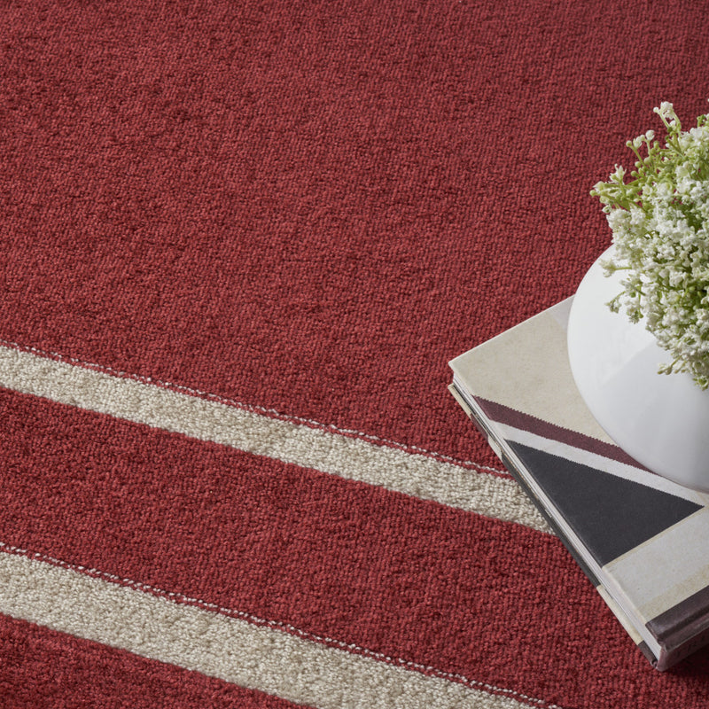Brick red rug texture with ivory border stripes; corner detail with a book display