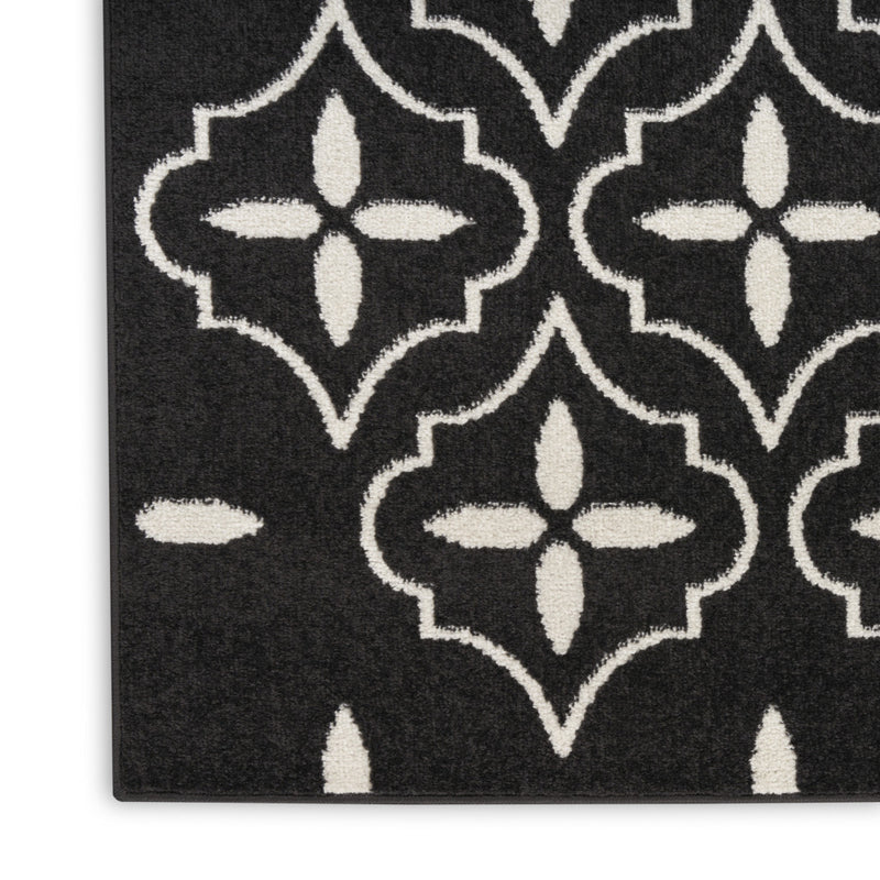 Corner view of black rug showing ivory quatrefoil shapes with looped outlines.