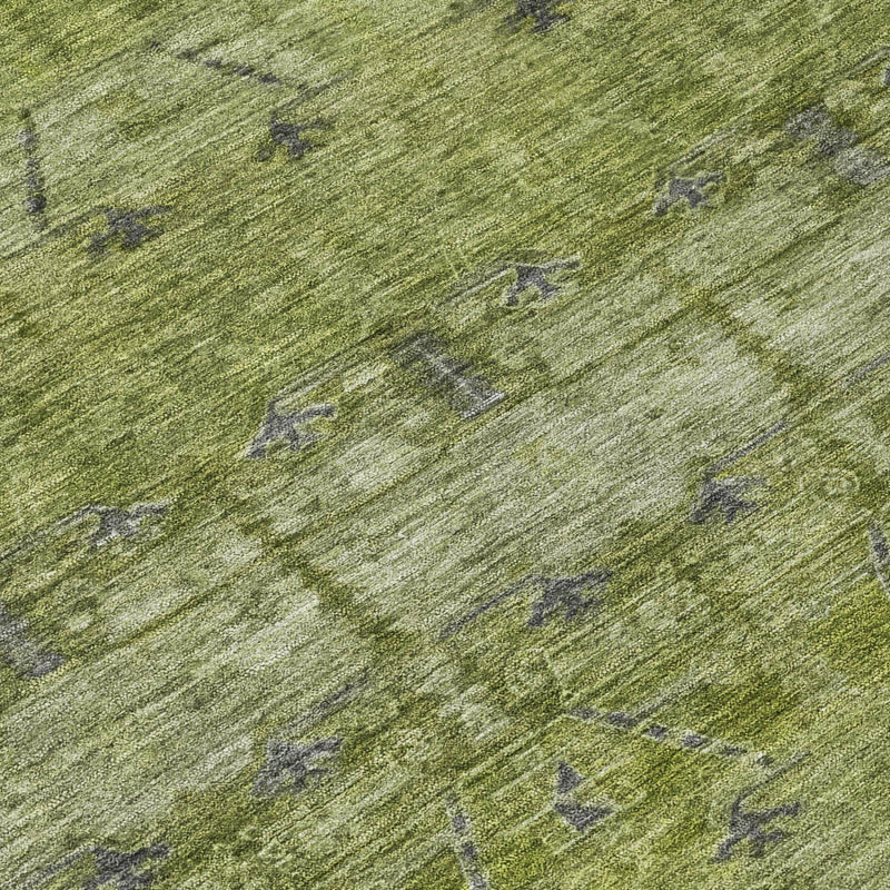 Olive green textured area rug with scattered tribal motifs and subtle dark speckling