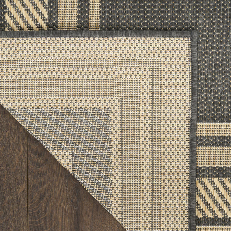 Charcoal area rug corner view with overlaid geometric border and stitched edge
