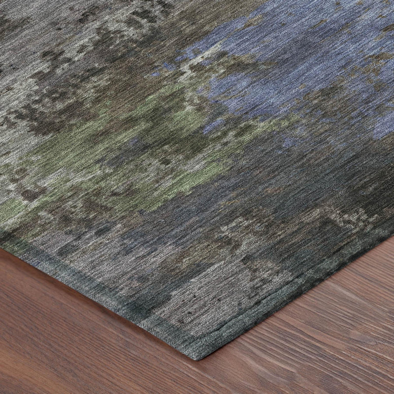 Corner of abstract area rug with distressed gray background and scattered blue and green marks.