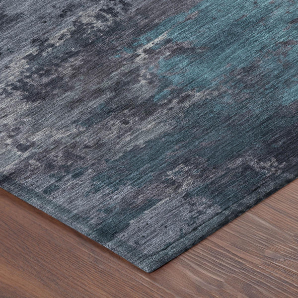 Abstract area rug with teal-blue and graphite washed pattern, angled corner view.