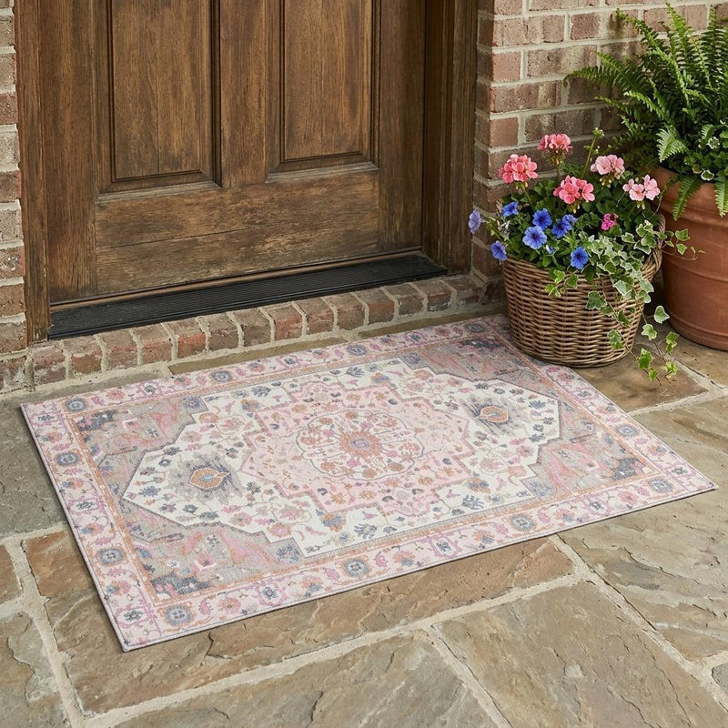 Pink and gray oriental indoor outdoor area rug laid on stone patio near a wooden door.