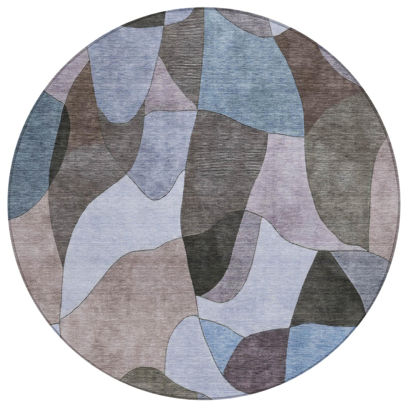 Round area rug with abstract patchwork pattern in light blue, beige, and charcoal gray.