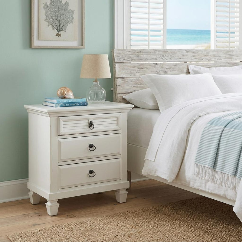 White wood 3-drawer nightstand beside bed with black ring pull handles