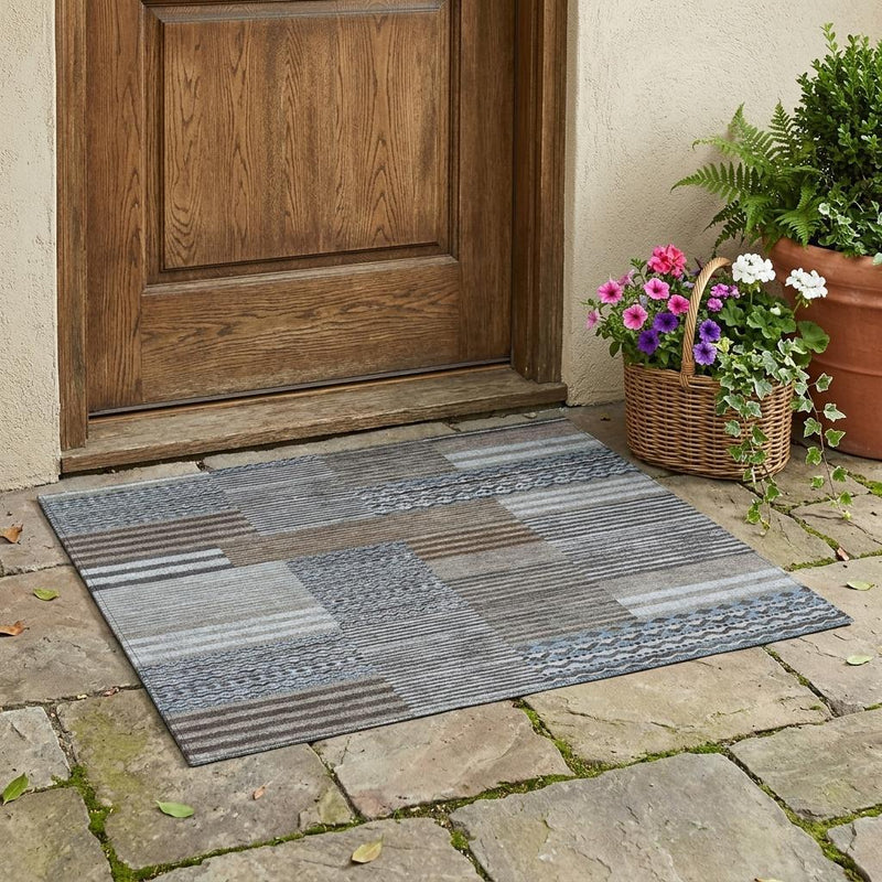 Indoor/outdoor area rug laid on stone patio, featuring gray and blue patchwork stripes